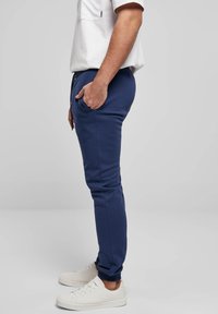 Tamsiai mėlyni treningai iš minkštos medžiagos, su siauru kirpimu, šoninėmis kišenėmis ir elastinėmis rankogaliais. Dėvimi su baltais sportbačiais.