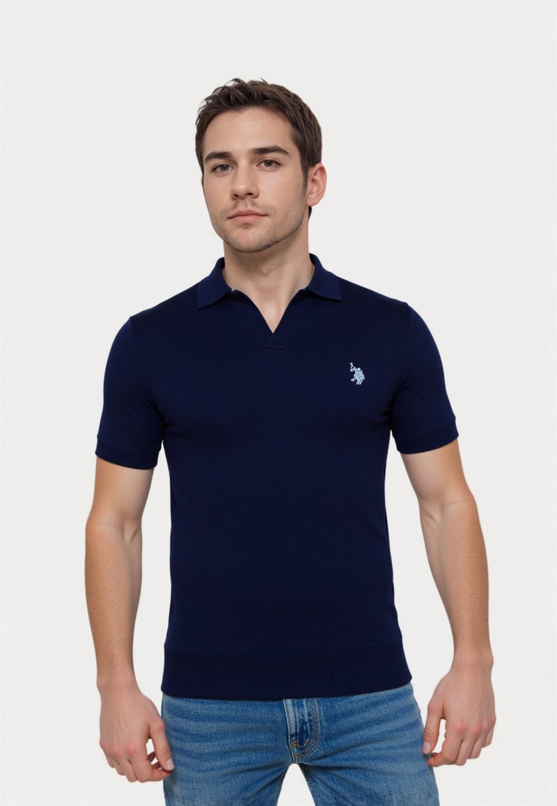 Camisa polo de color azul marino en un diseño ajustado, hecha de material acanalado con mangas cortas y cuello. Presenta un pequeño logotipo en el pecho.