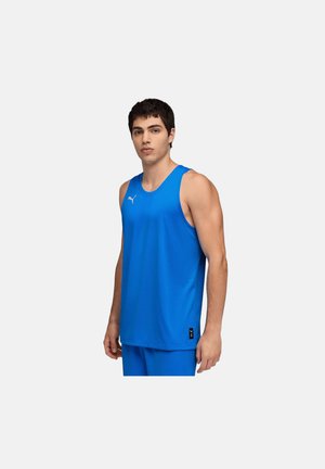 Mand iført en klarblå ærmeløs atletisk skjorte og matchende shorts, der står mod en ensartet lys baggrund.