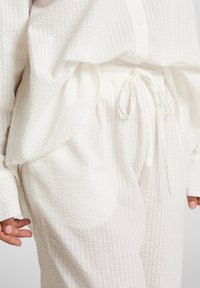 Witte gestreepte blouse en bijpassende broek met een elastische tailleband en trekkoord. De stof heeft een ruitpatroon.