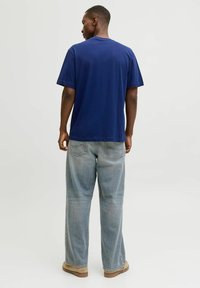 Camiseta de algodón azul marino de mangas cortas y cuello redondo, combinada con jeans de corte holgado azul claro. Calzado beige completa el conjunto.