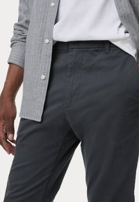 Donkerblauwe katoenen broek met een zachte textuur en zijzakken, gecombineerd met een lichtgrijze gestreepte overhemd met knopen.