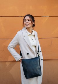 Schwarze Leder-Schultertasche mit glatter Textur, die ein schlichtes Design, einen verstellbaren Trageriemen und silberne Hardware-Akzente aufweist.