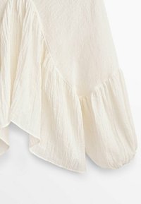 Haut en tissu blanc avec un ourlet froncé et un design léger et texturé. Le tissu semble doux et fluide, ce qui met en valeur sa drape.