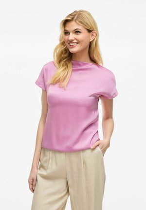 Blusa rosa a maniche corte con colletto alto e tessuto morbido e lucido. Abbinata a pantaloni beige chiaro, larghi.