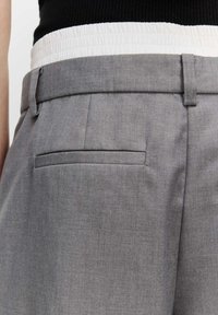 Graue maßgeschneiderte Hose mit glatter Textur, flachem Vorderteil, seitlichen Taschen und einem kontrastierenden weißen Bund.