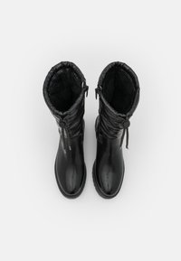 Botas negras impermeables con un acabado brillante, parte superior acolchada, cierre de cordón y forro interior texturizado. Suela de goma plana para un buen agarre.