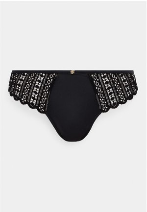 Culotte en dentelle noire avec motifs floraux sur les côtés, bords festonnés, et un petit pendentif logo doré centré sur la ceinture.