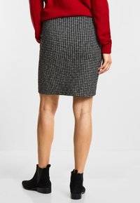 Schwarz-weißer Hahnentrittmuster-Bleistiftrock, knielang, mit taillierter Passform. Kombiniert mit einem roten Pullover und schwarzen Stiefeletten. Glatte Stofftextur.