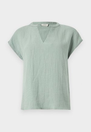Blouse courte en tissu texturé vert clair avec un col en V et une coupe décontractée sur un fond uni.