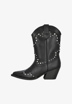 Bota de vaquero negra de cuero con puntera puntiaguda, costuras decorativas, tachuelas de plata y un tacón grueso. Presenta una lengüeta para facilitar su uso.