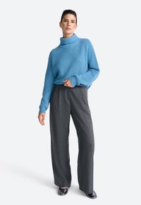 Pulover ribbed de un albastru deschis, cu guler înalt, asociat cu pantaloni evazați gri.Ținuta are o croială lejeră și o textură moale.