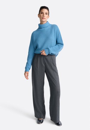 Suéter de canalé azul claro con cuello alto, combinado con pantalones de pierna ancha grises. El conjunto presenta un corte holgado y una textura suave.