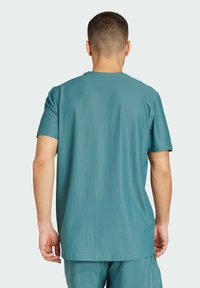 Chemise à manches courtes pour homme en bleu sarcelle doux, en tissu texturé, avec un col rond et une coupe décontractée, couture visible sur l'ourlet.