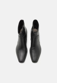 Crne kožne čizme do ankla s uskim vrhom i glatkom površinom. Imaju bočni patentni zatvarač i minimalne šavove za elegantan izgled.