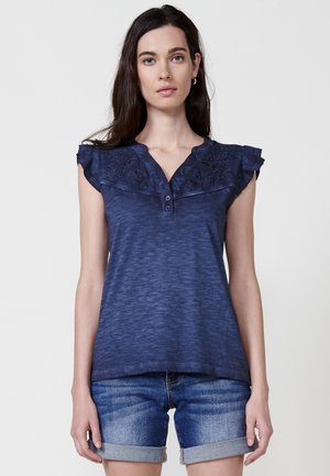 Top senza maniche blu navy in una morbida texture, con dettagli arricciati sulle spalle e ricami sul petto, con chiusura a bottone.