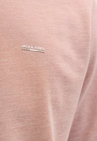 Chemise Jack & Jones rose clair avec un tissu texturé. Dispose d'un petit logo argenté sur la poitrine, mettant en valeur des éléments de design minimalistes.
