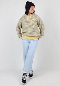 Sweat à capuche avec un motif en zigzag gris et jaune, doté d'une poche kangourou. Jean bleu clair à jambes larges et baskets noires.