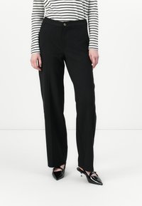 Pantalones negros ajustados con pierna recta, con cierre de botón y bolsillos laterales, combinados con una blusa de manga larga a rayas en blanco y negro.