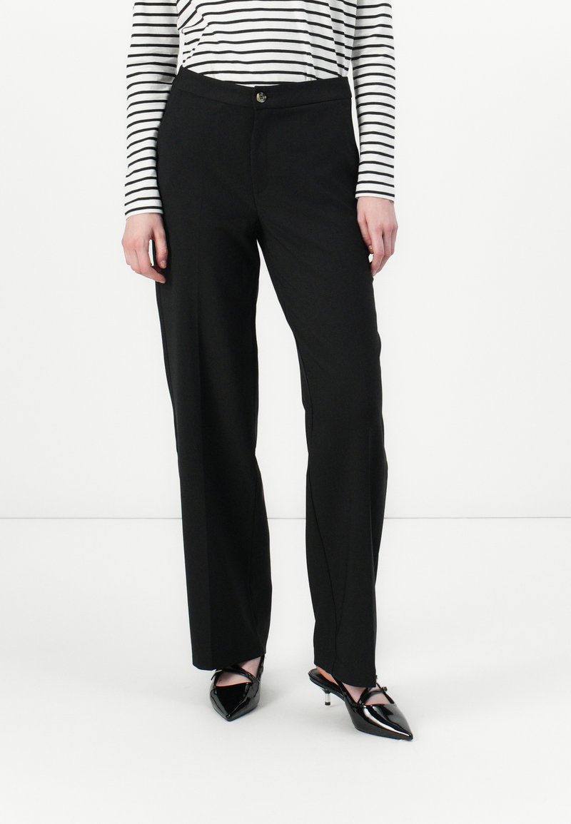 Pantalones negros ajustados con pierna recta, con cierre de botón y bolsillos laterales, combinados con una blusa de manga larga a rayas en blanco y negro.