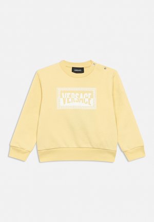 Light yellow long-sleeve sweatshirt with white Versace logo framed by Greek key pattern, featuring snap buttons on left shoulder.
