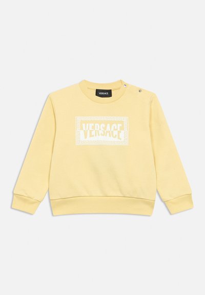 Sweat-shirt jaune clair à manches longues avec logo Versace blanc encadré par un motif clé grec, doté de boutons-pression sur l'épaule gauche.