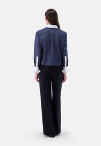 Navy cropped shirt with a white collar and cuffs, featuring button accents on sleeve opening. Paired with wide-leg black trousers.
