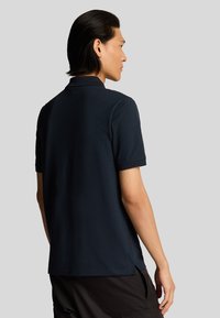 Polo de marina hecho de suave algodón, con un collar clásico, mangas cortas y aberturas laterales para mayor comodidad. Diseño minimalista.