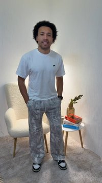 Λευκό κοντομάνικο μπλουζάκι με μικρό λογότυπο, γκρι φούτερ με σχέδιο, και μαύρα παπούτσια slip-on με άσπρες λεπτομέρειες, σε ένα ζεστό δωμάτιο.