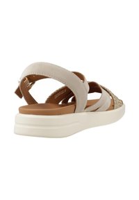 Beige sandal med tvärband och vävd detalj, med en dämpad tan fotbädd och en vit platåsål.