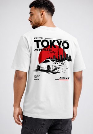 Man wearing white T-shirt with Tokyo skyline, drifting car, and Japanese text in black and red design on the back.