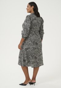 Vestido de patrón en blanco y negro con mangas largas, cintura ajustada y falda fluida. Presenta una tela texturizada y una longitud por debajo de la rodilla.