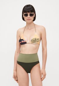 Top bikini a triangolo con motivo grafico arancione e giallo con la scritta "WILD." Slip alto in oliva e verde scuro con bordino arancione.
