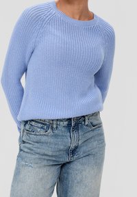 Hellblauer Strickpullover mit gerippter Textur, Rundhalsausschnitt und Raglanärmeln, kombiniert mit ausgewaschenen blauen Denim-Jeans.