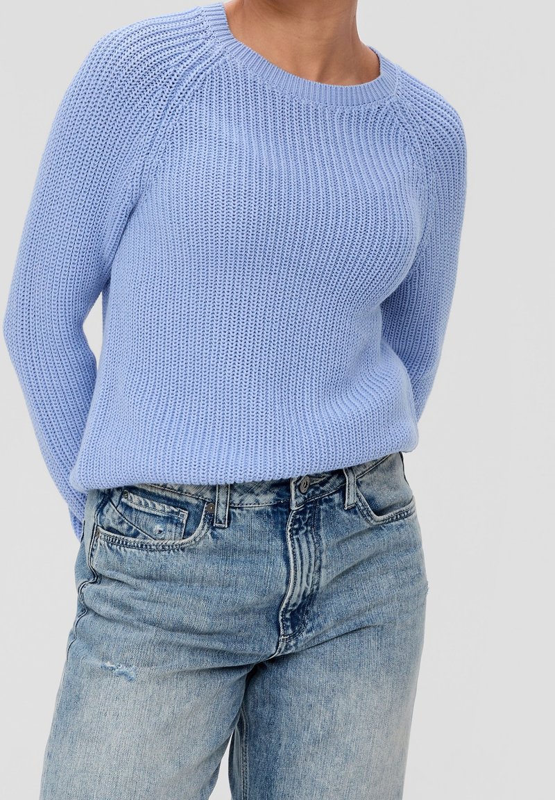 Hellblauer Strickpullover mit gerippter Textur, Rundhalsausschnitt und Raglanärmeln, kombiniert mit ausgewaschenen blauen Denim-Jeans.