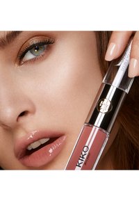 Lip gloss KIKO Milano in un tubo trasparente, con una tonalità rosa-pink e un accento metallico. Il modello mostra labbra lucide e smalto per unghie neutro.