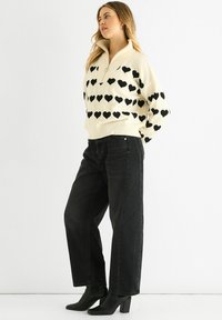 Cream sweater with black heart patterns, half-zip collar; paired with high-waisted black jeans and black block-heel ankle boots.