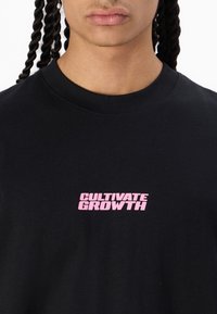 Black cotton t-shirt featuring a prominent pink "CULTIVATE GROWTH" print on the front. Crew neck design with a smooth texture.