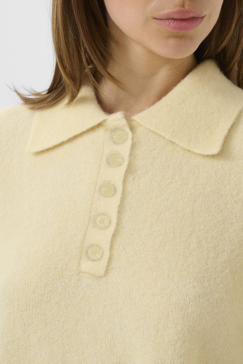 Femme portant un pull jaune pâle duveteux avec un col pointu et une rangée verticale de cinq boutons assortis.