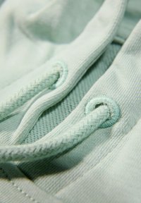 Tela verde claro con una textura suave presenta cordones trenzados y ojales. Primer plano que muestra el intrincado bordado y los detalles del material.