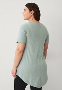 Lys grøn kortærmet tunika med rund kant og glat tekstur. Detalje med bagsøm og afslappet pasform, parret med sorte leggings.