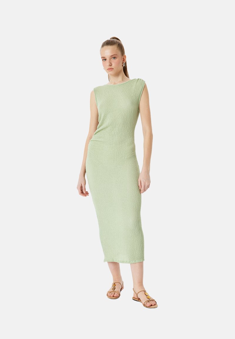 Grünes strukturiertes Strick-Midikleid mit kurzen Ärmeln und figurbetontem Schnitt. Kombiniert mit braunen flachen Sandalen.