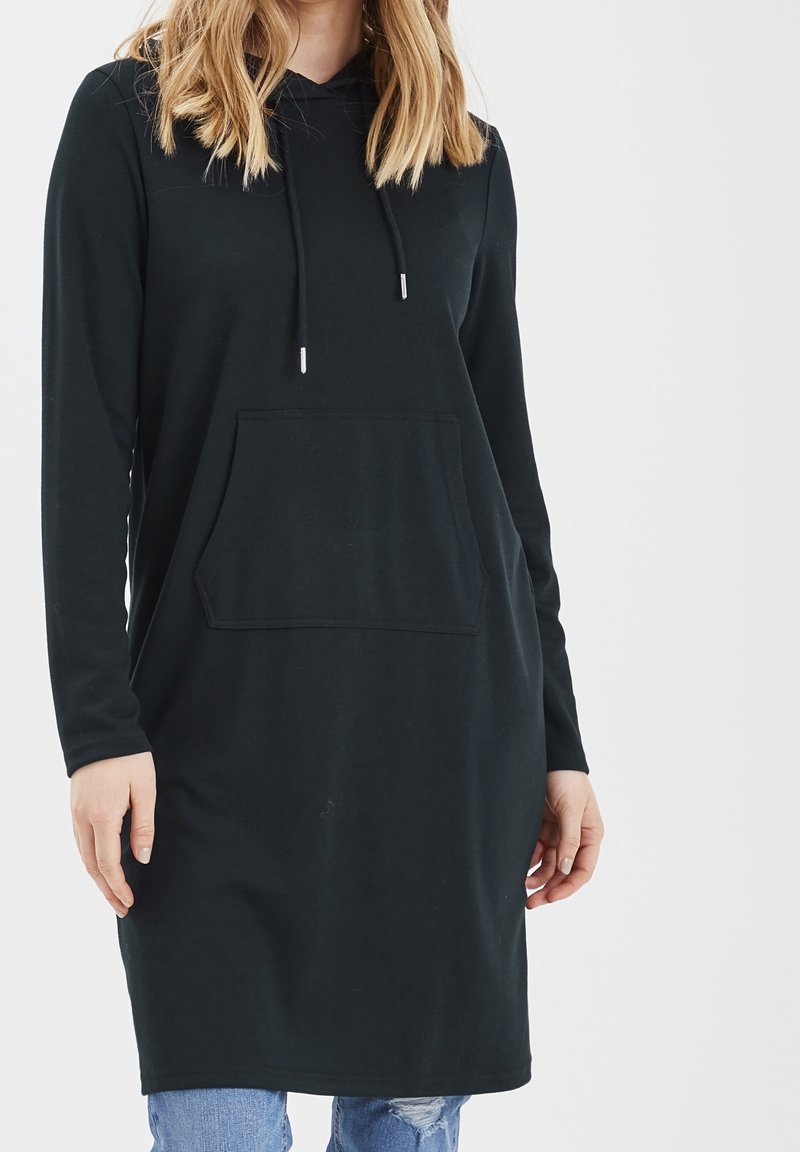 Svart huvtröja klänning i mjukt tyg, med långa ärmar, en framficka och en avslappnad passform, som når ovanför knäna.