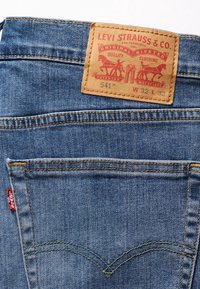Poche arrière d’un jean en denim bleu avec une étiquette en cuir Levi Strauss & Co indiquant la taille W32 L32 et une étiquette en tissu rouge Levi’s.