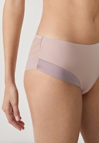Hipster de mujer en color púrpura claro, con textura suave, diseño sin costuras y un panel con rayas horizontales en un lado.