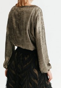 Metalický bronzový top s dlouhým rukávem a texturovaným povrchem, s kulatým výstřihem a volným střihem, doplněný černou sukní s třásněmi.