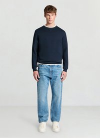 Sweat-shirt bleu marine à col rond, poignets et ourlet côtelés, associé à un jean droit bleu clair et des baskets blanches sur un fond neutre.