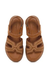 Sandalias de ante marrón con diseño recortado, acentos de tachuelas y correas ajustables. Plantillas de cuero suave y suelas texturizadas.