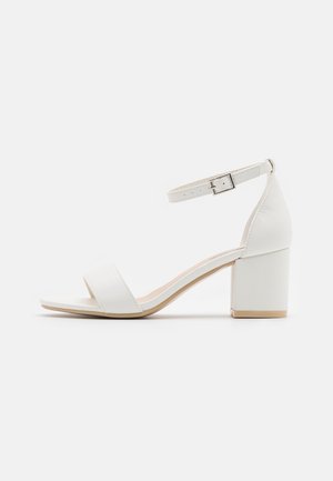 Sandale à talon haut blanche avec un bout carré, devant ouvert, sangle de cheville et un talon bloc. Matière en cuir lisse, design minimaliste.