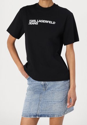 Osoba nosząca czarną koszulkę Karl Lagerfeld Jeans oraz jasnoniebieską dżinsową mini spódnicę z subtelnym wzorem w kratę.